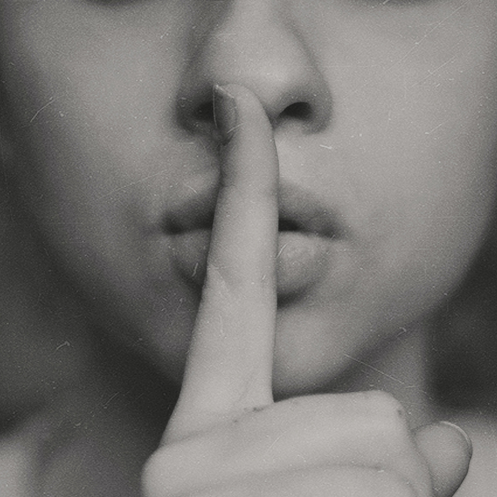 a woman holds her finger to her lips in a "shh" motion